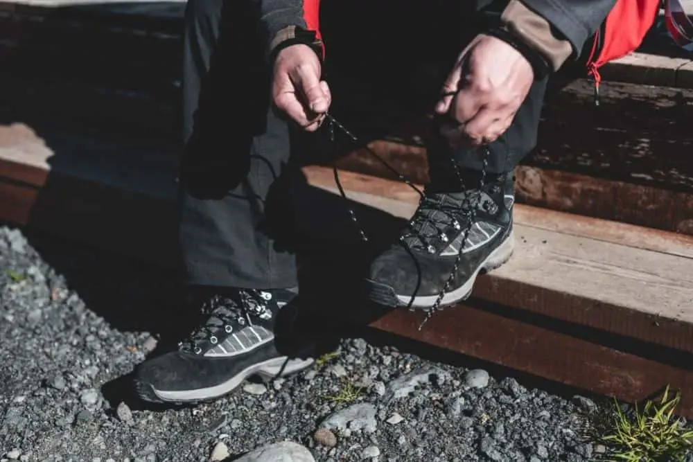 man tightens shoelaces of hiking boots to prevent stones getting into