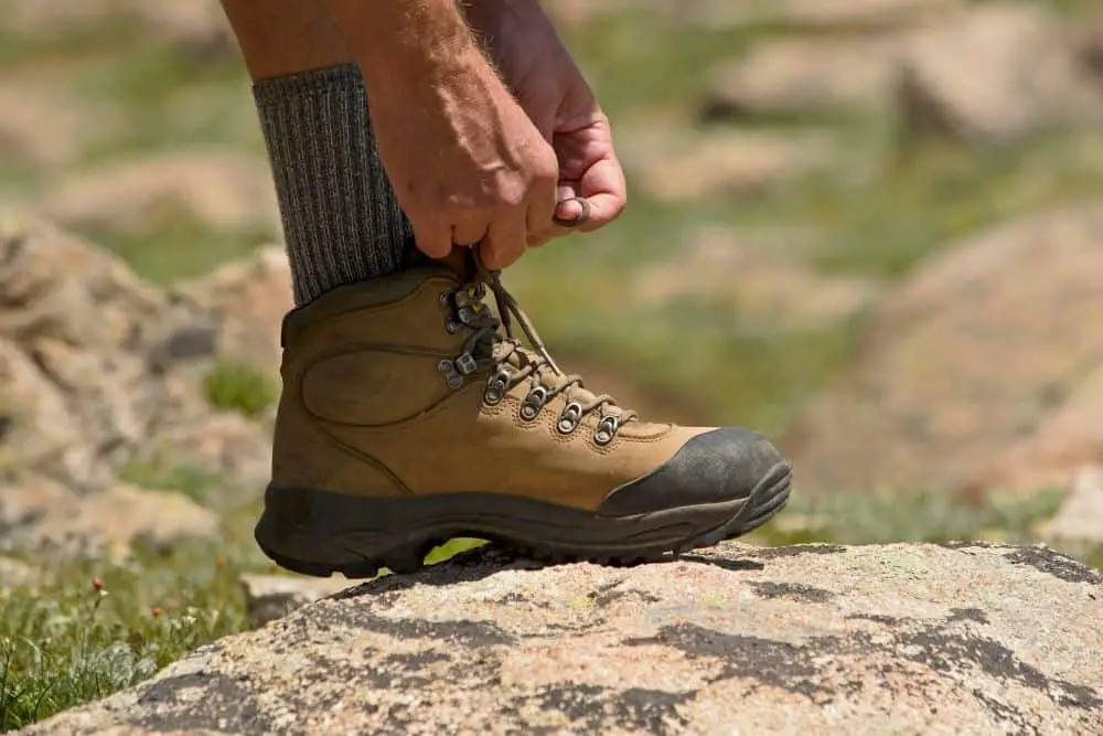 men stand one legs on the rock and tying the lace of hiking boots