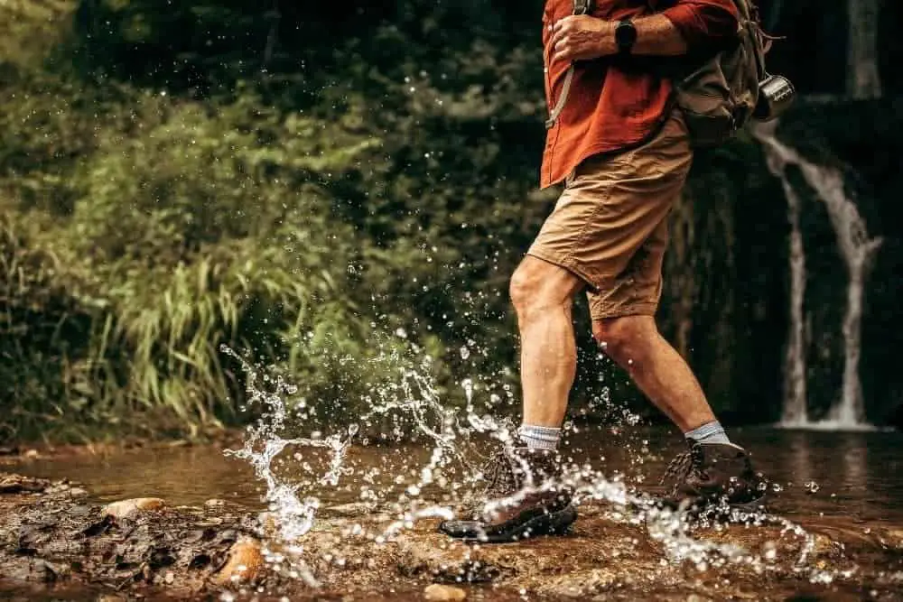 man hiking through a natural waterfall with water splashes on his waterproof hiking boots
