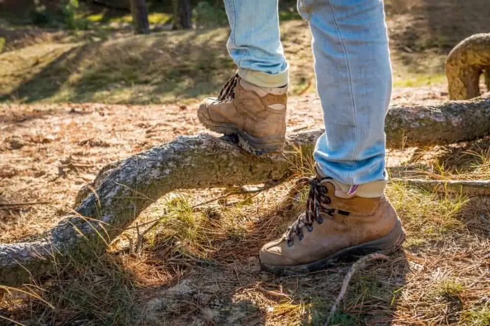 man wearing hiking boots with heels standing on a fallen branch