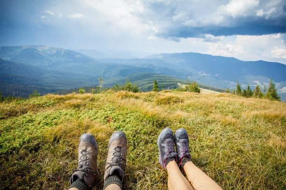 two people wearing broken in hiking boots sitting on a mountain