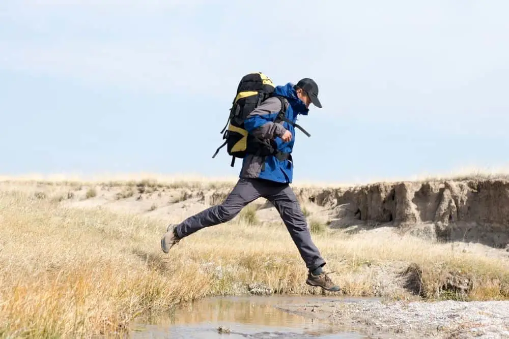 man wearing dark pants and hiking boots jumping through a puddle