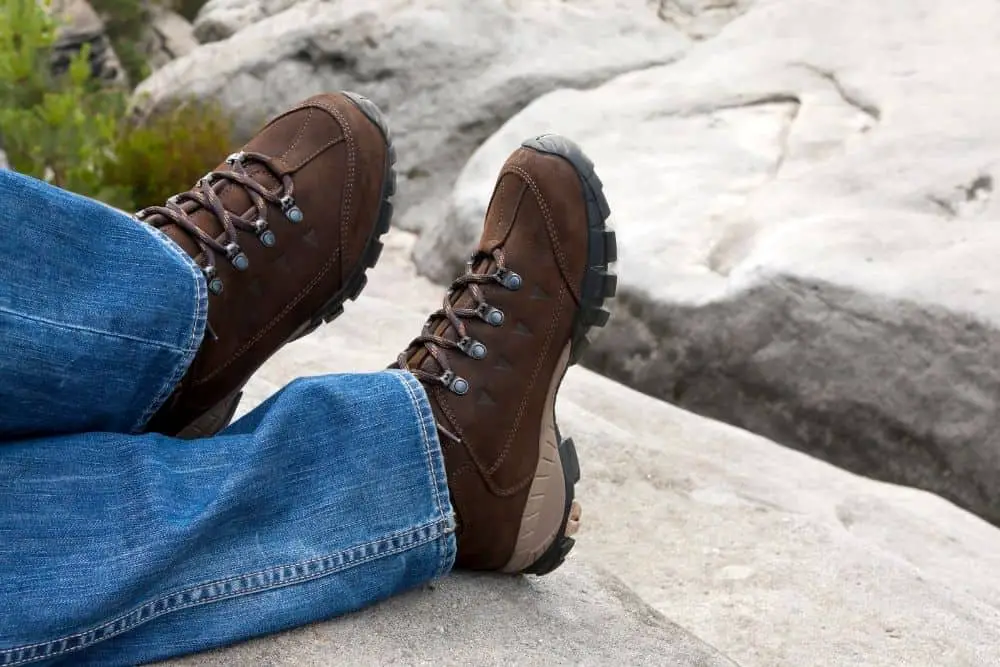 man wearing jeans and brown hiking boots sitting on a big rock