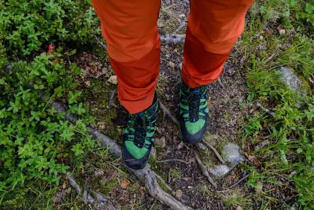 orange pants are tuck in green hiking boots in a forest