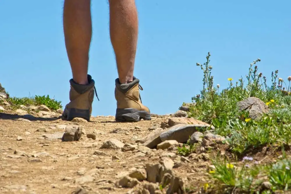 man wearing hiking boots standing on terrain with sand and tiny stones