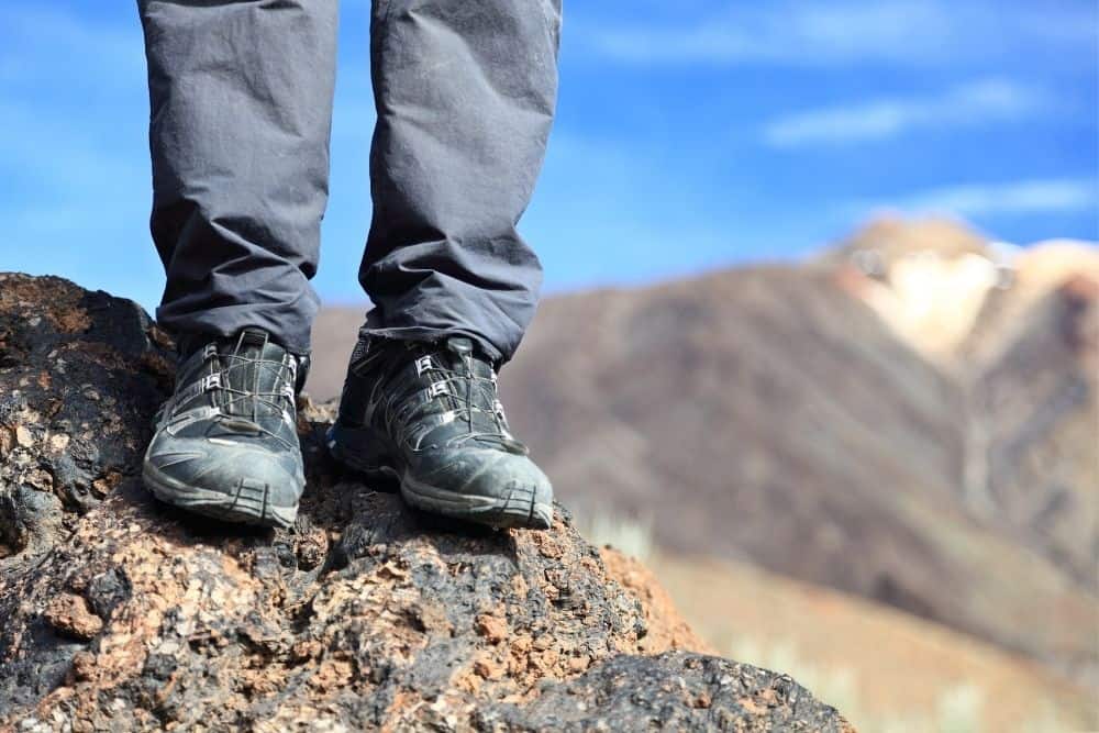 man wears hiking boots and gray pants standing on rock