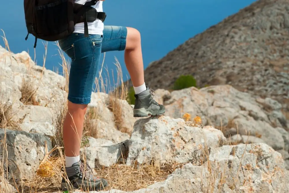 woman with black backpack wearing hiking boots standing on rock