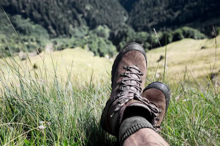 a man is wearing hiking boots with gray socks sitting on the grass