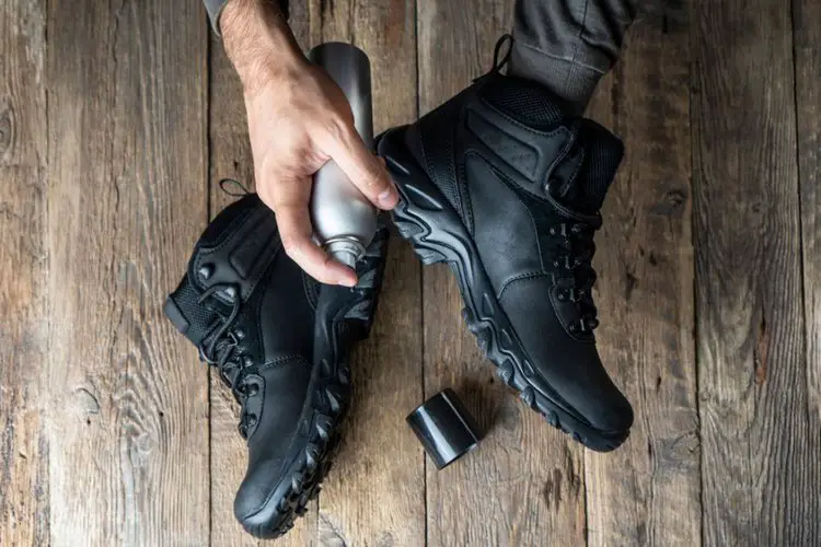 man using spray to waterproof black hiking boots