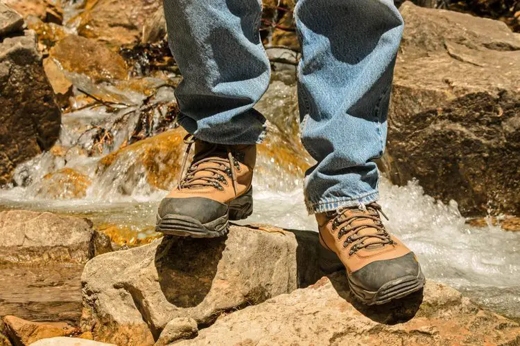 man wears hiking boots standing near the stream