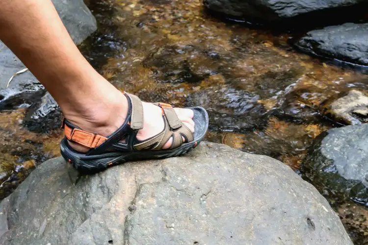 man wears sport hiking sandals crossing a stream