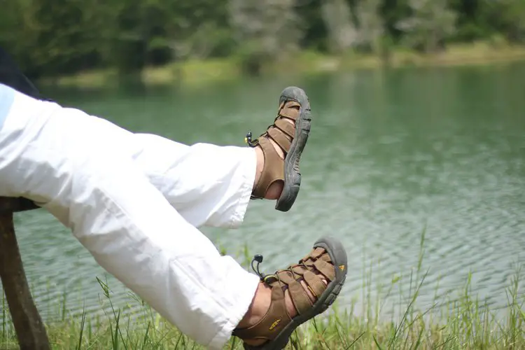man wears water hiking sandals sitting near a lake