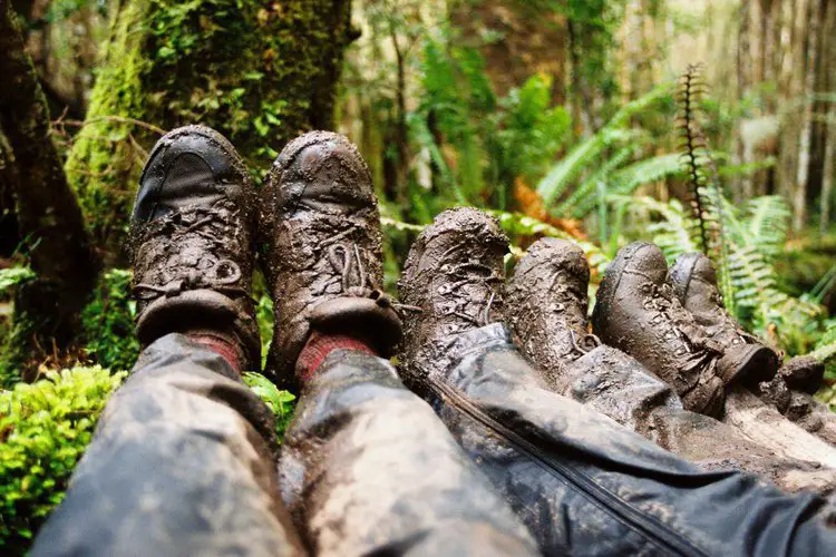 three pairs of hiking boots with wet mud in the forest