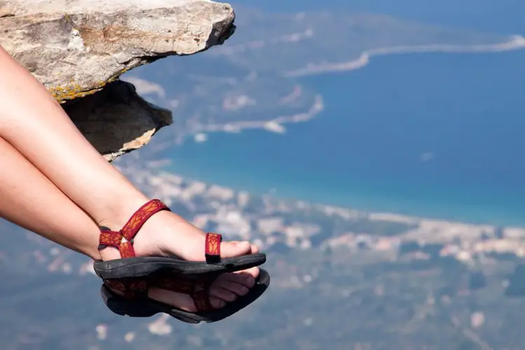 woman wears hiking sandals sitting on a cliff