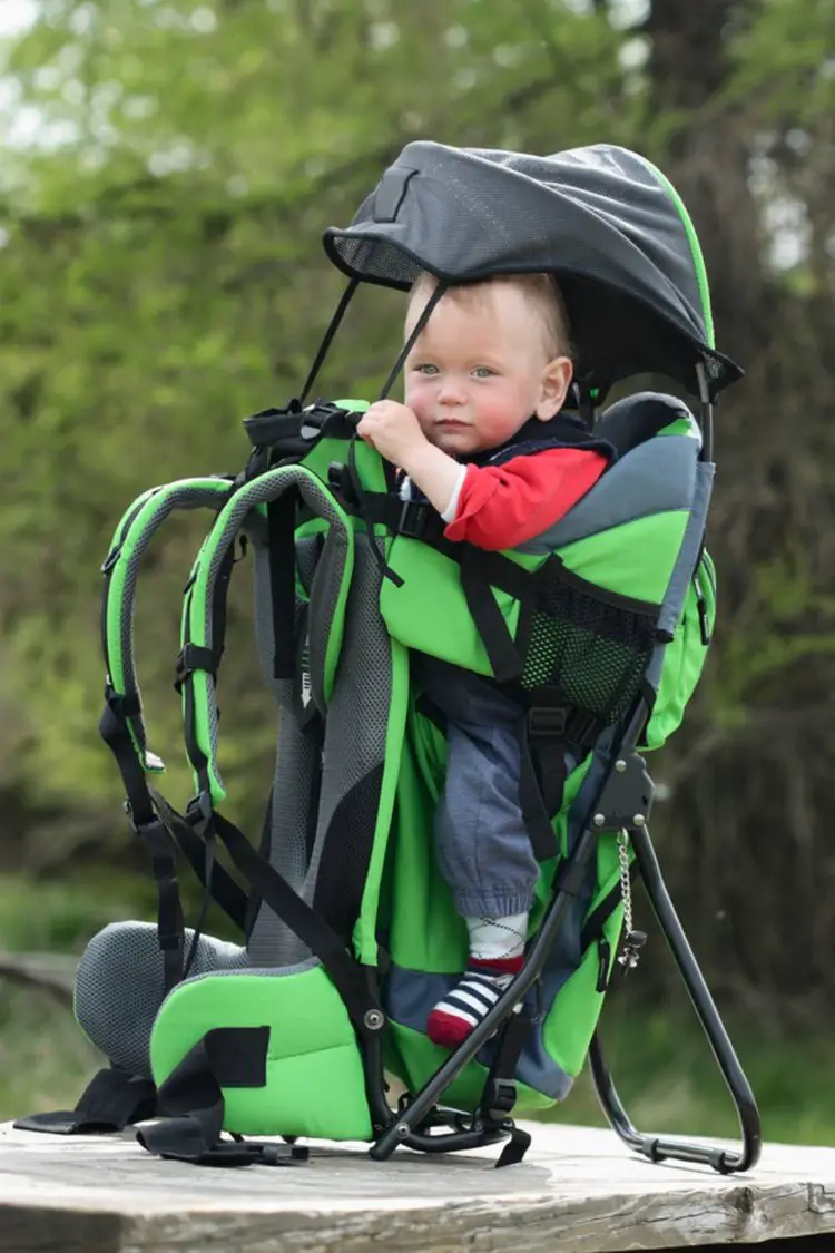 a baby in a green baby hiking backpack