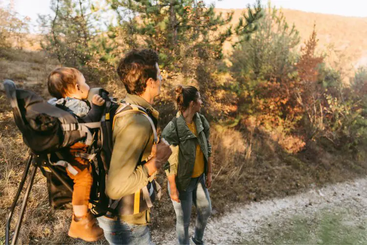 a couple carries their baby in hiking backpack