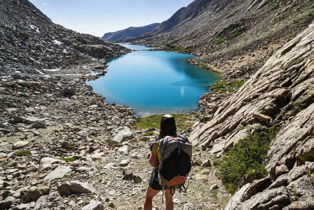 a girl is hiking on rocky terrain with a big hiking backpack