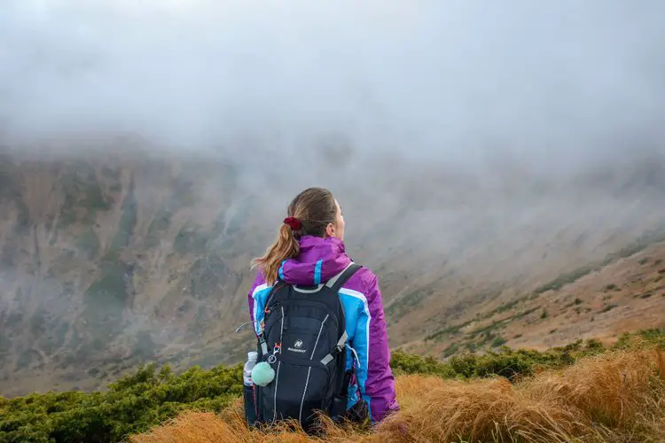 a girl with small hiking backpack sitting on a mountain peak