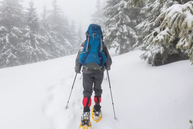 a man is hiking on thick snow with blue big hiking backpack