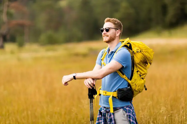 a man is wearing a yellow hiking backpack on the field