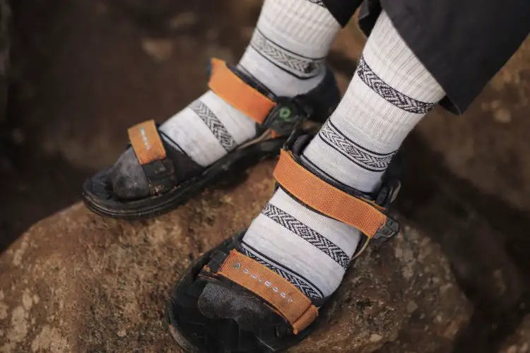 a person wears thin socks with hiking sandals on a rock
