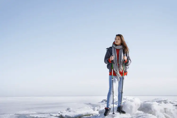 girl stands with hiking poles on snowy terrain