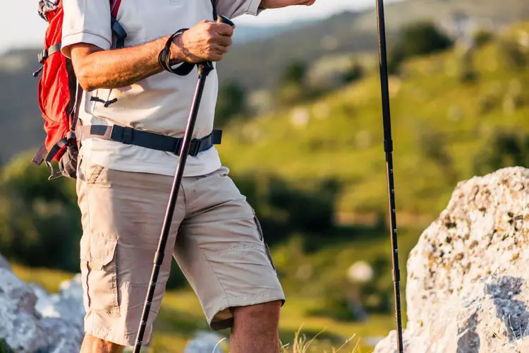 man uses hiking straps on hiking poles on rocky terrain