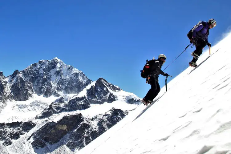 Two people are climbing a steep snow-covered mountain