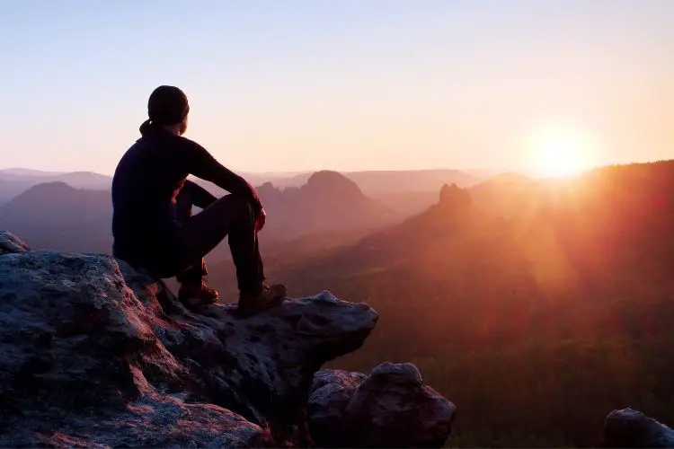 a hiker contemplates sunrise in a mountain