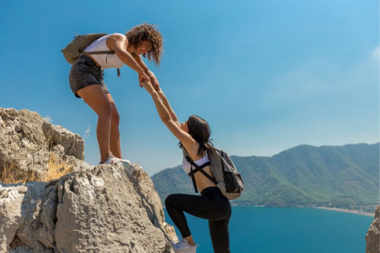 a woman is pulling her friend from a rock