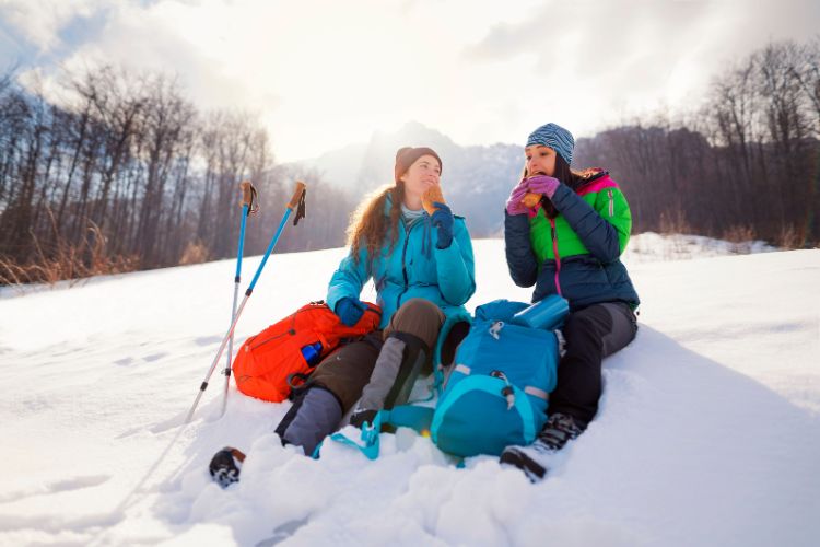 two women hiking in the winter are eating