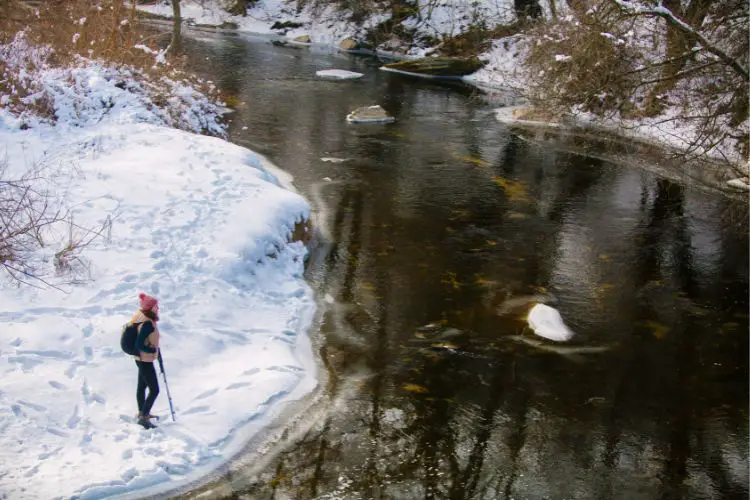 woman is going hiking and standing near a lake with snow around