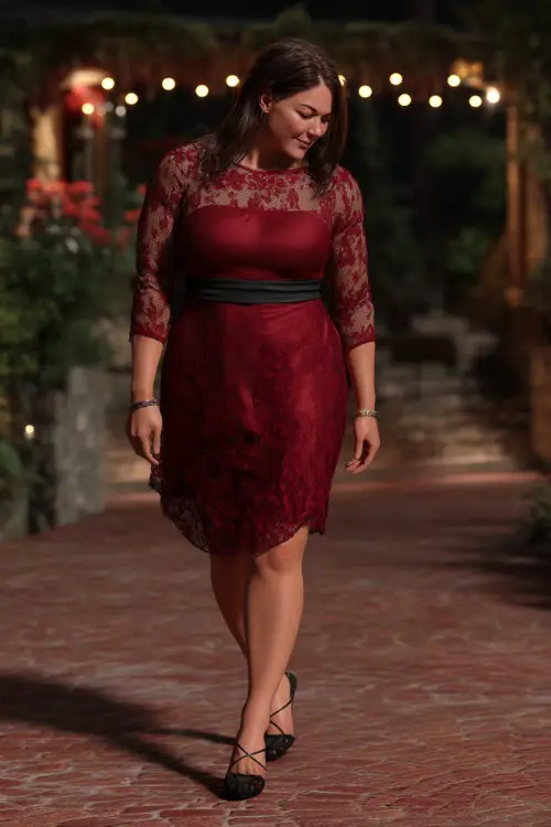 A confident plus-size woman over 50 in a burgundy cocktail dress with lace sleeves and black heels, walking on a brick path at a romantic evening wedding