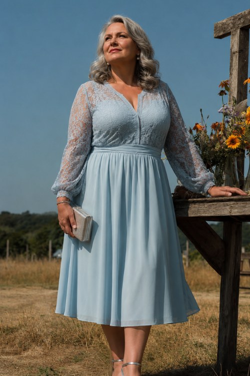 A plus-size woman over 50 in a pastel blue midi dress with a lace bodice and flared skirt, posing by a simple outdoor altar with wildflowers