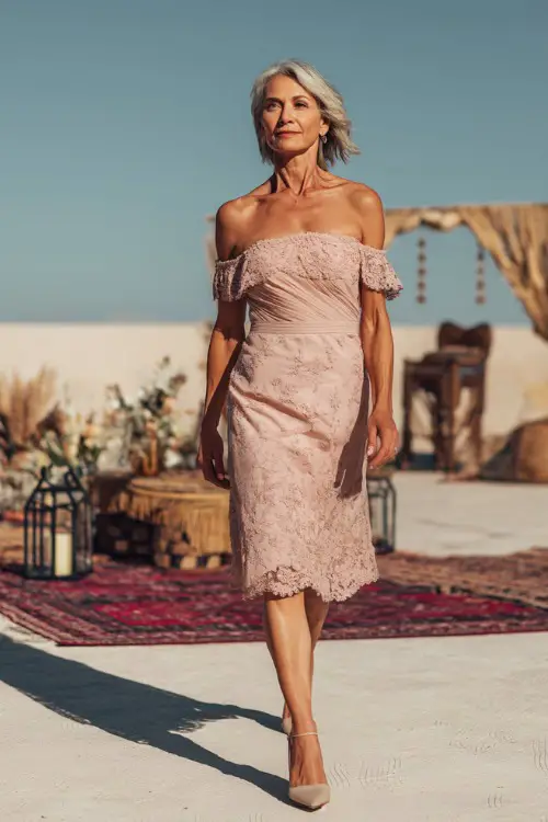 A poised woman over 50 wearing a blush pink off-the-shoulder midi dress with delicate floral embroidery and heels