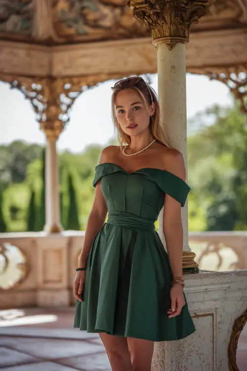 A woman in a forest green off-the-shoulder cocktail dress with a structured bodice and pearl accessories, standing beneath an ornate gazebo at a luxury summer venue 