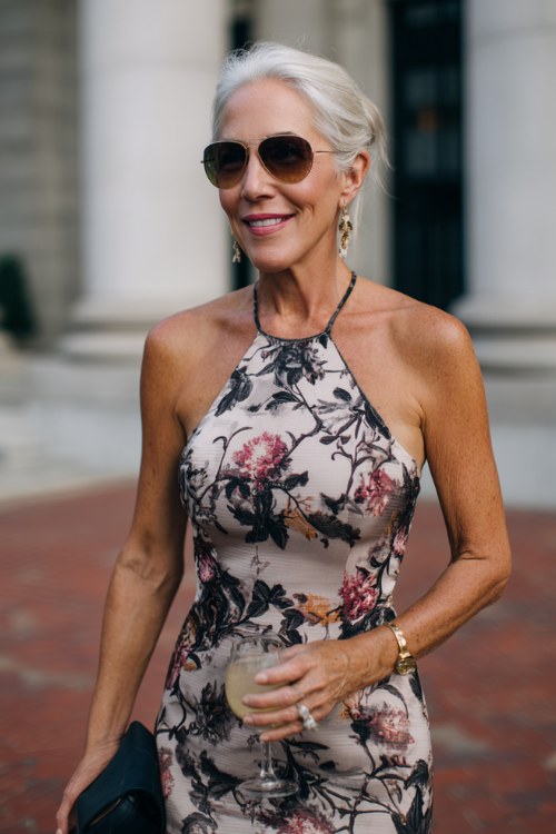 a woman over 50 wears a floral halter cocktail wedding guest dress