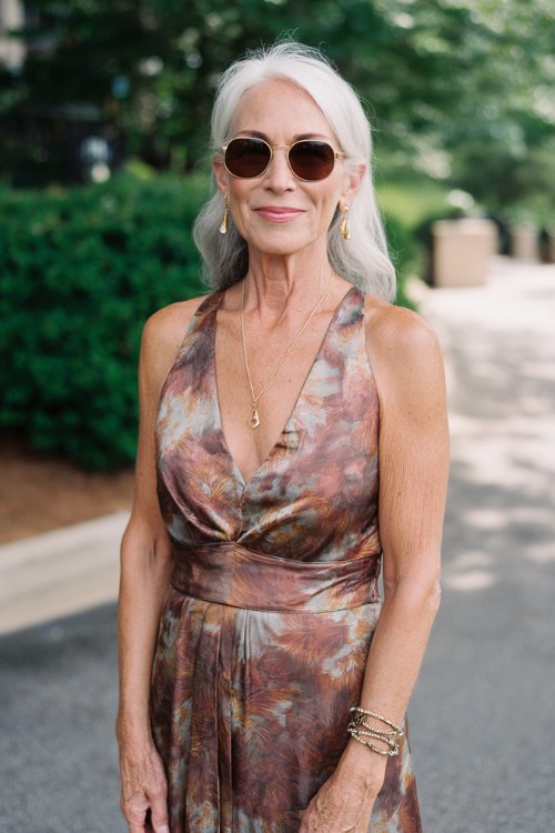 a woman over 50 wears a summer wedding guest dress with halter neckline and fitted waist