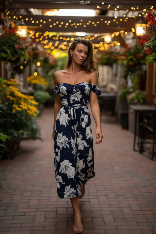 A confident woman in a navy blue dress with large white floral prints and short sleeves, walking through a patio surrounded by summer blooms and fairy lights 