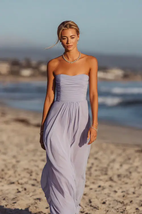 A confident woman in a pale lilac strapless chiffon gown with a structured bodice and minimal jewelry, walking across the sand at a formal coastal wedding