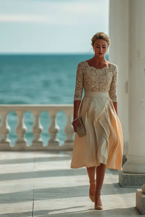 A graceful woman in a light champagne A-line dress with lace sleeves and a pearl clutch, walking through a formal rehearsal space at an oceanfront estate 