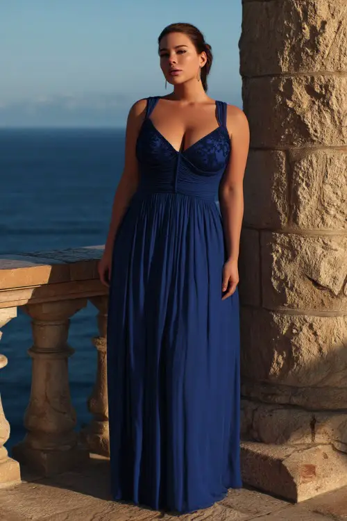 A plus-size woman in a royal blue formal gown with a sweetheart neckline and chiffon overlay, standing on a stone balcony at sunset with ocean views