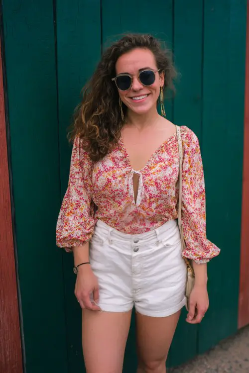A midsize woman wears a flowy floral blouse with white shorts