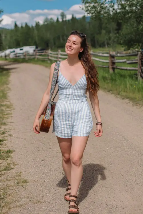 A midsize woman wears a striped romper with a deep neckline and flat sandals