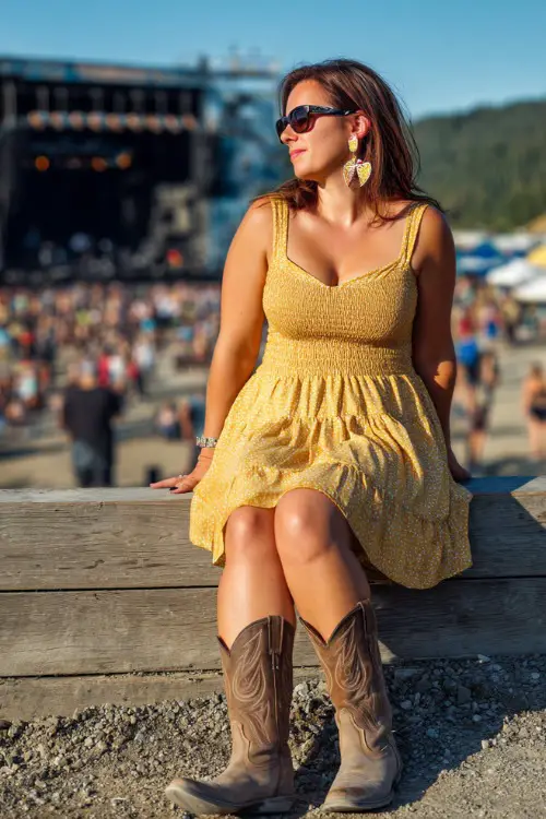 A plus-size woman wearing a smocked midi sundress in sunflower yellow with classic western boots, styled with statement earrings and sunglasses 