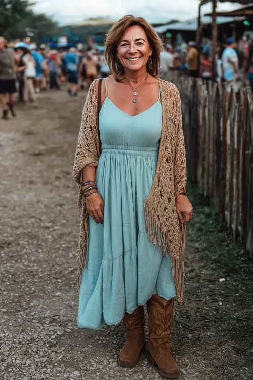 A woman over 50 wearing a breezy sleeveless maxi dress in soft turquoise, layered with a lightweight crochet shawl and suede ankle boots