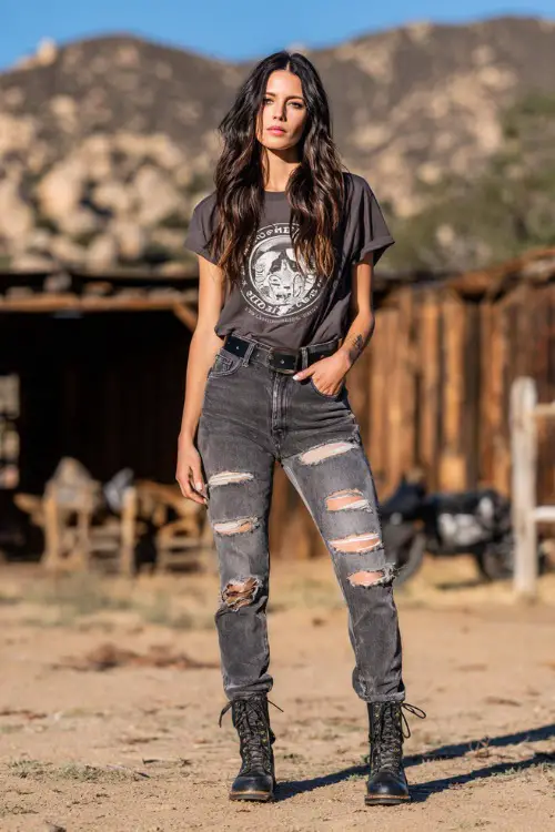A woman wearing a loose-fitting band tee tucked into ripped skinny jeans, accessorized with a black belt and combat boots 