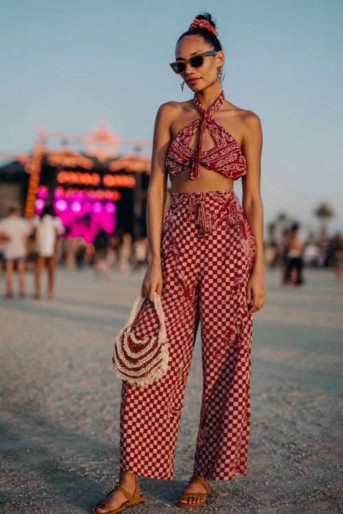 A woman wears a cropped bandana-print halter top in classic red and white, and matching high-waisted wide-leg trousers and sandals