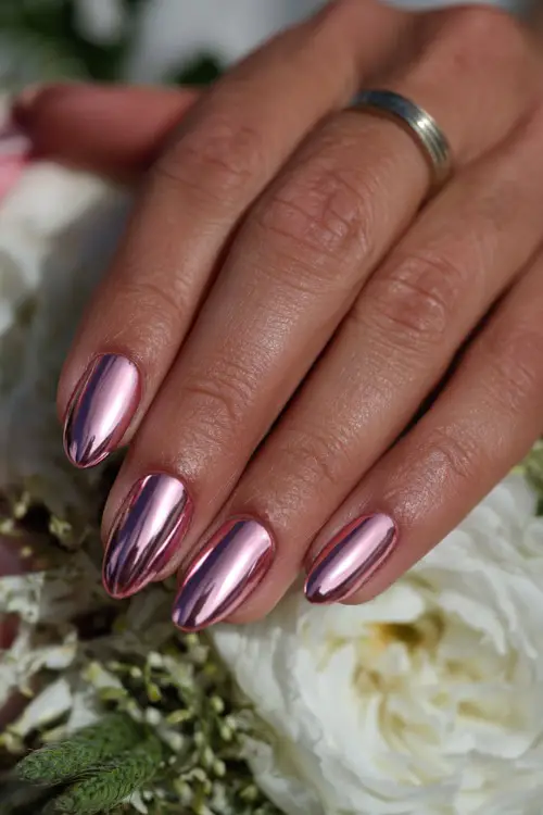 Acrylic bridal nails with full chrome mirror finish in rose pink, almond-shaped, hand softly placed on wedding table setup 