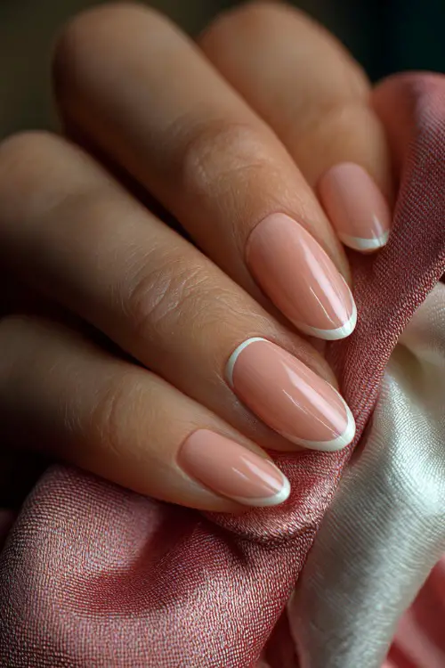 Bridal fingers gently pulling on silk glove, almond-shaped nails in pastel peach-pink with a fine white French outline